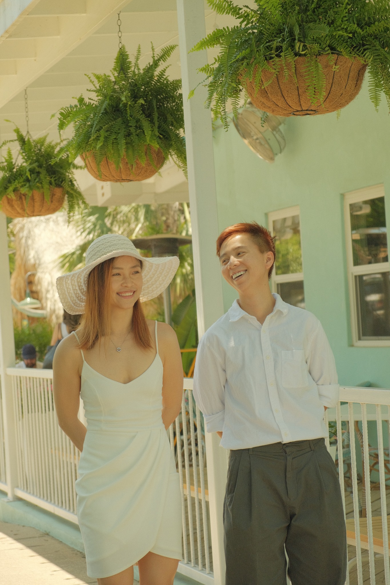 A couple smiling under hanging plants on a sunny porch